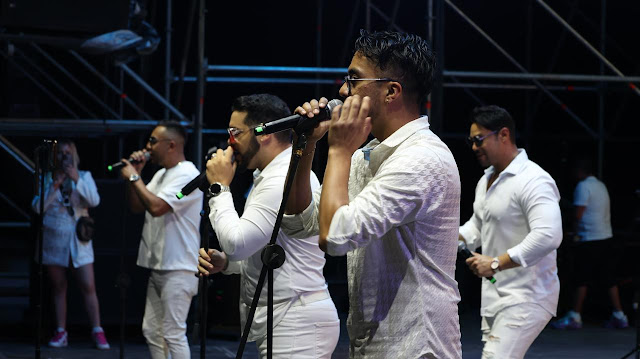 Personas con camisas blancas estan cantando en un lugar que para como teatro. Tambien vino el consul honorario de alemania en Queretaro Marco Schachtner y esta applaudando.